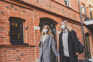 Naklejka premium Young pretty girls friends in medical masks having fun outdoor in autumn evening in city laughing - end of pandemic concept