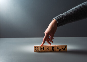 hand posing wooden blocks QMS, Quality management system concept. system for achieving quality...