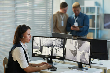 Side view portrait of young woman wearing headset while watching surveillance camera feed in...
