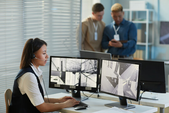Side view portrait of young woman wearing headset while watching surveillance camera feed in security and monitoring office, copy space - Powered by Adobe
