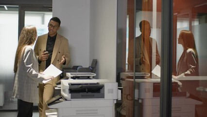 Two young multiethnic colleagues is copying documents at office standing near copier machine 