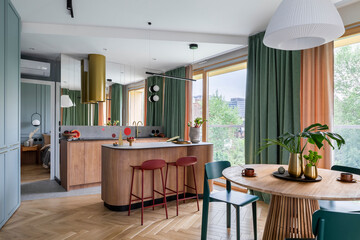 Interior design of harmonized dining room with kitchen, round table, green chairs, wooden kitchen...