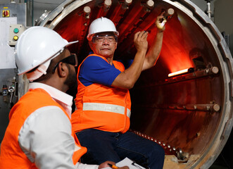 Two professional male engineers wearing hard hats working to inspect and maintain machinery...