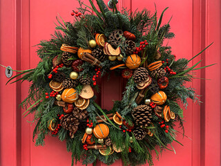 Selective focus of Christmas wreath. Festive christmasy themed winter natural wreath on a pink wooden door, decorated with lotus, pine cones, oranges, vanilla stick. Red berries. Festive mood.