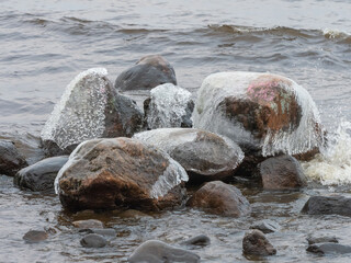 Transparent ice and ice icicles on stones on the shore of the Onega Lake in Karelia in autumn after frost