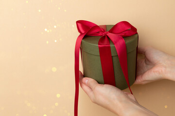 New Year and Christmas background. Female hands holds green round gift with red ribbon on a yellow background. Front view