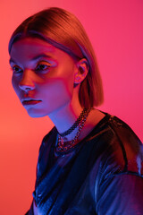 portrait of trendy woman in necklaces posing in neon light on coral and pink background.