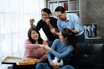 Group of Asian man and woman friends watching soccer games world cup competition on television with...