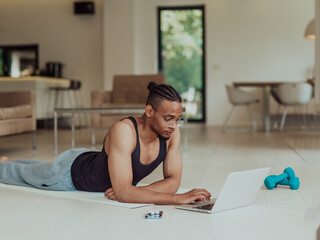 Training At Home. Sporty man doing training while watching online tutorial on laptop, exercising in living room, free space