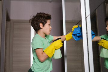 boy with inspiration cleans the house, washes the mirror with a spray and a sponge. the mantesori system, the child participates in simple household chores.