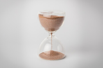 Horizontal view of an hourglass or sandglass shot with studio illumination against a white background. The passage of time is visible through the glass as it races by and sand falls from top to bottom