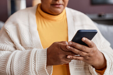 Close up of black senior woman holding smartphone and chatting online at home