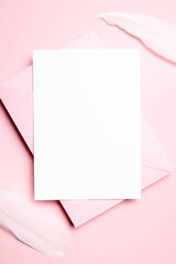 Holiday greeting card mockup with pink envelope and white feather on light pink background, top view, flat lay. Blank wedding invitation or Valentine Day letter, empty card