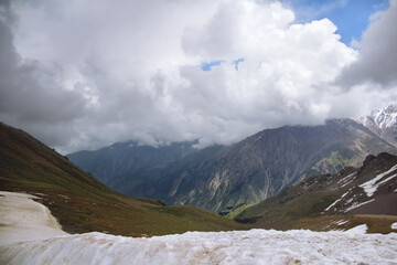 Mountain range with peaks, thick clouds on the peaks, sunlight on the slopes, snow in the foreground, Chimbulak mountain resort, winter