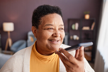 Portrait of black senior woman recording voice message to family via smartphone and smiling