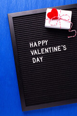 St. Valentines day card. Letterboard with congratulation phrase  and box with present and hearts  oh bright blue paper textured background. Top view.