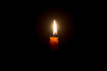 A single burning candle flame or light glowing on a beautiful spiral orange candle on black or dark...