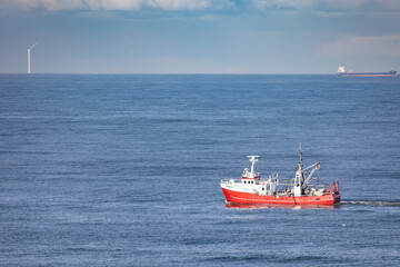 A red cutter on the North sea with a cargo ship and a wind turbine in the background