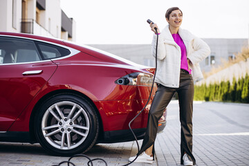 Woman standing by electric car holding charging pistol