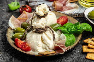 Italian tomatoes and burrata cheese salad served with cherry tomatoes, fresh basil leaves, prosciutto ham and olives on a light background. Restaurant menu top view