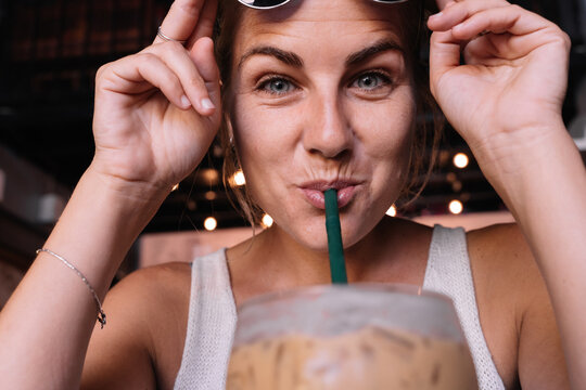 Close up portrait of a woman drinking iced coffee with a straw