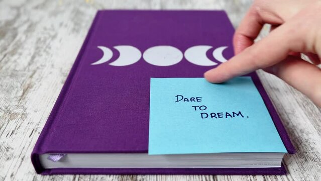 Hand placing a post-it note with message "dare to dream" on diary