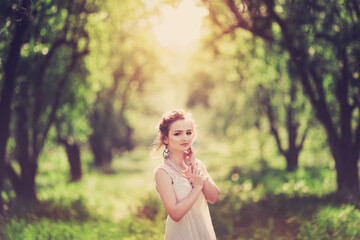 Beautiful blonde slender girl in a vintage look with a cape walks along the spring arch, sunset