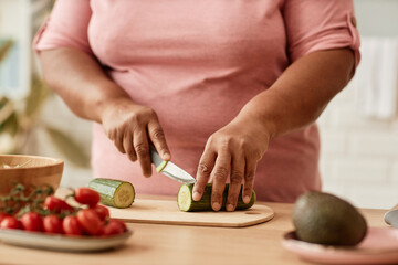 Close up of overweight black woman cutting vegetables while cooking in kitchen