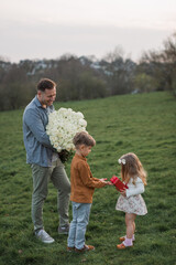 Fototapeta premium Happy little child boy gives smiling girl a gift box, making a surprise. Happy little girl is holding gift in red box and smiling, daddy holding flower