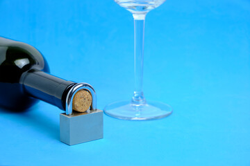 Glass and bottle wine with lock on neck on blue background.Concept ban on drinking, prohibition.