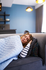 Obraz premium Girl sleeps on cozy sofa in living room at siesta time under a warm blanket. Sleeping woman taking nap on the sofa during the day.