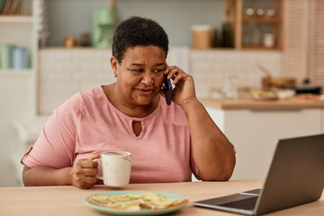 Fototapeta na wymiar Warm toned portrait of black senior woman talking on phone while enjoying breakfast in morning