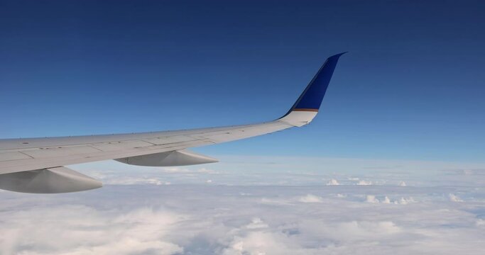 In background of fluffy cloudy sky, an airplane wing is seen flying above clouds skies from window