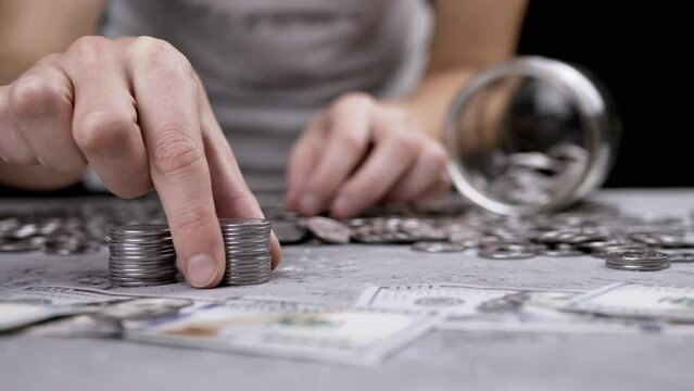 Female Hands Building a Tower from a Stack of Coins near scattered money. Glass jar, piggy bank. Hand places silver cent on top of a tower. Budget, spending, savings, accumulation. Wealth, poverty.