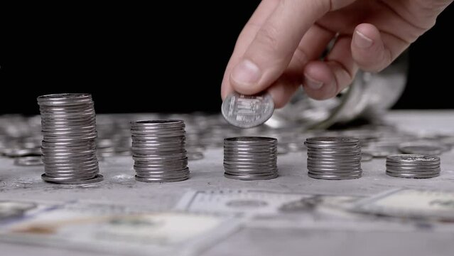 Female Hands Building a Tower from a Stack of Coins near scattered money. Glass jar, piggy bank. Hand places one silver cent on top of a tower. Budget, spending, savings, accumulation. Finance. Cash.