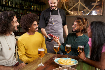 Customer making wireless or contactless payment using smartphone in a bar. Store worker accepting payment over NFC technology.