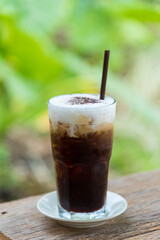 Tasty iced coffee in glass  served with  milk and ice cubes on wood table, nature background.