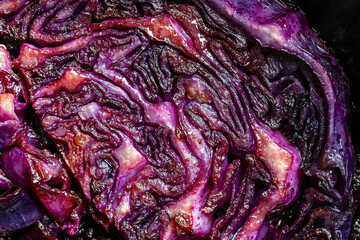 Obraz premium Red cabbage wedges are pan-fried until lightly charred, then braised in mulled wine. Background of fry blue cabbage in a section, macro. Texture and pattern of purple cabbage