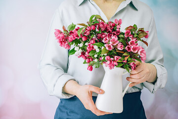 Hands of woman florist in apron holds a bunch of magenta pink spring flowers. Midsection. No face. Springtime gardening. Mothers day. Bouquet of viva flowers on blue Copy space.