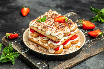 homemade tiramisu cake with fresh strawberry, mascarpone and mint. Tiramisu portion on plate on dark background. Delicious no bake tiramisu