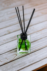 Aroma diffuser with green perfume in a glass bottle with sticks close-up on a wooden background.