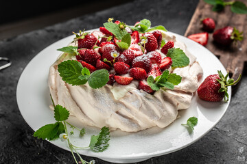 Homemade delicious meringue cake Pavlova with whipped cream, fresh strawberries and mint on wooden...