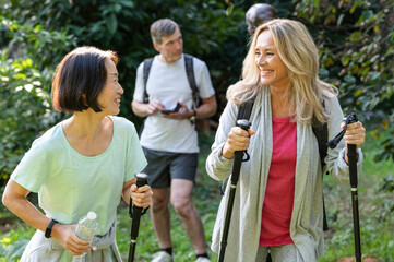 Two middle-aged ladies with hiking poles walking in the woods with their partners behind them