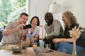 Senior man sharing pictures on smart phone with friends while sitting on sofa