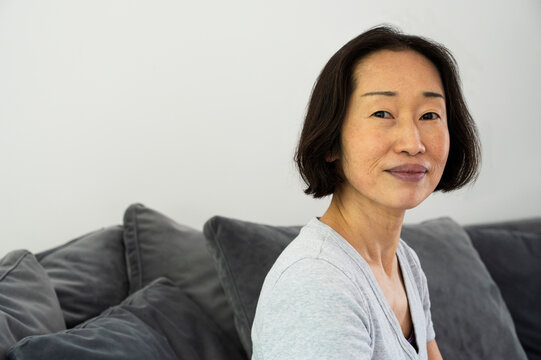 Portrait of Asian-American senior woman looking at camera and sitting in living room - Powered by Adobe