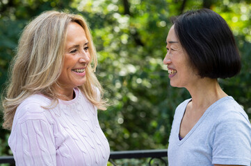 Side view shot of senior Asian-American woman and her friend smiling at each other while standing outdoors