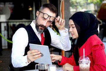 Senior elderly mature business man with wow excited surprised face having coffee in caffe and talking with headscarf hijab Muslim women, happy harmony people take a break from drinking beverage.