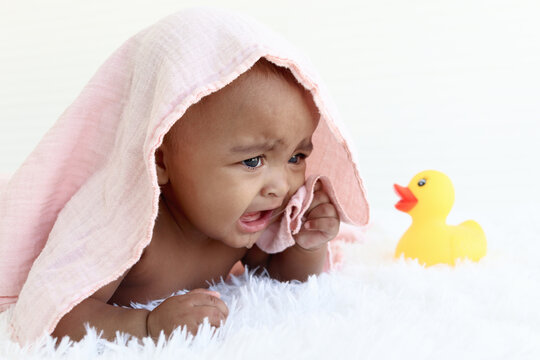 Portrait of adorable six month crawling African American baby covered in towel after bath time, happy smiling sweet little girl kid playing with yellow duck toy, childhood and baby care concept.