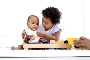 African American curly hair girl trying to feed her little sister with spoon of food, infant eating healthy homemade baby food, daughter help mother to look after baby kid, childhood baby care concept