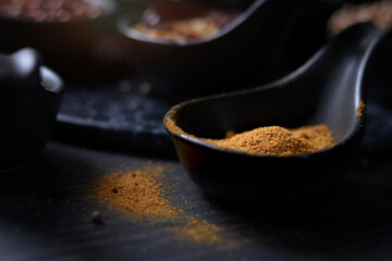 Spices and herbs on dark background, yellow turmeric powderin tablespoon with assorted colorful of seasoning ingredients as blurred background